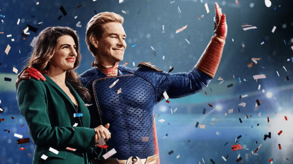 A woman in a green blazer smiles and holds the arm of a man dressed in a superhero costume, reminiscent of The Boys Season 4. The man waves with his other hand as confetti falls around them, creating an energetic atmosphere that screams celebration.